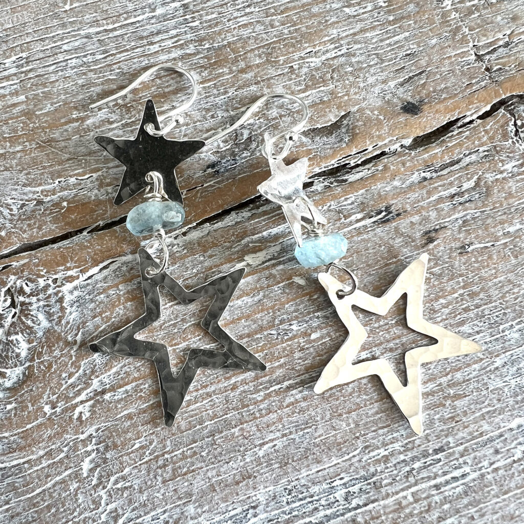 Adur Art Collective jewellery artwork by member artist Jo Kirby, Star Earrings in silver against a wood background.