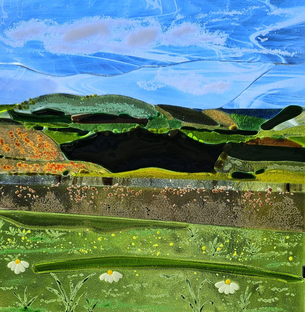 Adur Art Collective glass fusion artwork by member artist Sarah Jane Bridgland, depicts the landscape of Cissbury Ring looking to the South, artwork has blue sky at the top and green and black hills below.